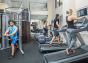 Thumbnail 24 of 38 - Fitness center with treadmills and lat pull machine. People running on treadmill and using stationary bicycle at The Bartram Apartments in Gainesville, FL 32608