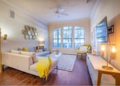 Thumbnail 31 of 38 - Living room space with dark brown vinyl wood floors and L shaped couch and TV mounted on the right side of the wall at The Bartram Apartments in Gainesville, FL 32608