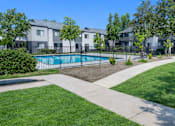 Thumbnail 19 of 19 - A swimming pool is surrounded by a grassy area and apartment buildings.