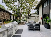 Thumbnail 2 of 16 - A patio with a table and chairs is surrounded by a stone wall and trees.