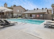 Thumbnail 6 of 21 - A pool area with sun loungers and a building in the background.