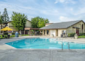 Thumbnail 14 of 14 - A large swimming pool in front of a building with a yellow umbrella and a black fence.