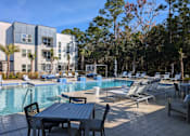 Thumbnail 21 of 30 - A pool area with chairs and a table in front of a building.