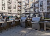 Thumbnail 10 of 31 - a group of stainless steel barbecue grills in an outdoor patio with an apartment building