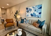 Thumbnail 23 of 30 - A living room with a grey couch, a brown armchair, a coffee table, and a large blue and white painting on the wall.