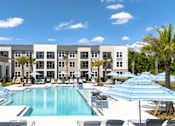 Thumbnail 37 of 62 - A large swimming pool surrounded by lounge chairs and umbrellas in front of a multi-story building.