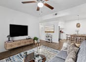 Thumbnail 1 of 33 - A living room with a grey sofa, a wooden coffee table, a flat screen TV, and a ceiling fan at Riviera Park, Chandler Arizona
