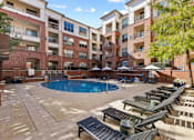 Thumbnail 19 of 25 - A large outdoor pool area with sun loungers and umbrellas in front of apartment buildings.