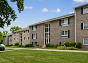 Thumbnail 27 of 40 - Multistory brick apartment buildings with manicured lawn at The Brook At Columbia Apartments, Columbia, MD