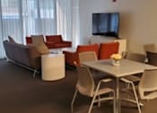 Thumbnail 4 of 8 - A modern living room with a grey sofa, red chairs, and a white coffee table.