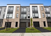 Thumbnail 6 of 8 - A modern apartment building with a black and white facade and a small tree in front.