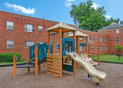 Thumbnail 15 of 18 - a child playing on a playground in front of a brick building at Hamilton Manor Apartments, Hyattsville, Maryland