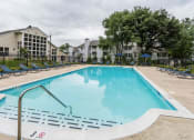 Thumbnail 23 of 35 - a swimming pool with chaise lounge chairs and apartment buildings in the background at Madison at Eden Brook, Columbia, MD