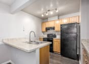 Thumbnail 12 of 56 - A kitchen with a black refrigerator, sink, and wooden cabinets at Madison at Eden Brook, 21046