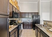 Thumbnail 4 of 24 - A kitchen with black appliances and brown cabinets at Prairie Crossing, Farmers Branch, 75244