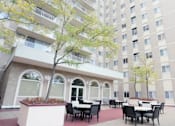 Thumbnail 9 of 10 - A patio with tables and chairs is surrounded by a building.