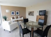 Thumbnail 1 of 10 - A living room with a glass table surrounded by black chairs.