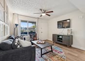 Thumbnail 8 of 33 - A living room with a grey couch, a coffee table, and a ceiling fan at Riviera Park, Chandler Arizona