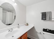 Thumbnail 10 of 40 - Modern bathroom with white countertop and oval mirror at The Brook At Columbia Apartments, Maryland