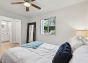 Thumbnail 15 of 33 - A bedroom with a bed, a ceiling fan, and a window with a view of trees at Riviera Park, Chandler Arizona