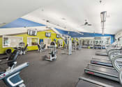 Thumbnail 20 of 54 - a gym with cardio equipment and weights on the floor and a yellow and blue wall at Villages at Morgan Metro, Landover, 20785