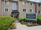 Thumbnail 26 of 40 - Leasing center entrance with monument sign and flowers at The Brook At Columbia Apartments, Columbia, Maryland