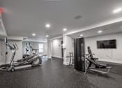 Thumbnail 31 of 46 - A spacious gym with treadmills, elliptical machines, and a television.