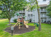 Thumbnail 41 of 46 - A playground with a slide and a tree in front of apartment buildings.