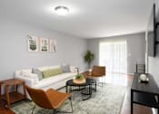 Thumbnail 12 of 65 - A living room with a white couch, a brown chair, a black table, and a television on the wall.