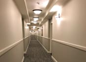Thumbnail 6 of 26 - A long hallway with carpeted floors and white walls.