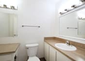 Thumbnail 36 of 47 - A white toilet sits in a bathroom with a sink and mirror.