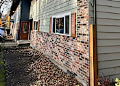 Thumbnail 12 of 47 - A house with a grey siding and a brick chimney.