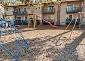 Thumbnail 13 of 47 - A playground with a blue swing set and a red slide in front of apartment buildings.