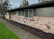 Thumbnail 8 of 25 - A building with a grey roof and a brick wall with a small garden in front.