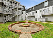 Thumbnail 17 of 25 - A courtyard with a brick fire pit surrounded by apartment buildings.