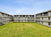 Thumbnail 4 of 25 - A large grassy courtyard in front of apartment buildings.