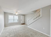Thumbnail 16 of 25 - A room with a carpeted floor, a ceiling fan, and a staircase.
