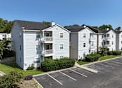 Thumbnail 27 of 29 - A row of white apartment buildings with a parking lot in front at Sedgefield Square Apartments, Greensboro, 27407