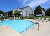 Thumbnail 17 of 29 - A swimming pool with a metal railing and lounge chairs in front of a large apartment building at Sedgefield Square Apartments, Greensboro