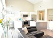 Thumbnail 14 of 29 - A black leather couch sits in a modern kitchen with white cabinets and appliances at Sedgefield Square Apartments, Greensboro, North Carolina