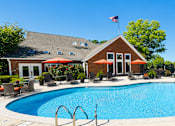 Thumbnail 9 of 18 - A pool with a red umbrella and a building in the background.