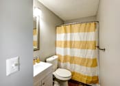 Thumbnail 8 of 29 - A bathroom with a toilet, sink, and striped shower curtain at Sedgefield Square Apartments, North Carolina, 27407