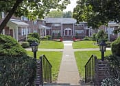 Thumbnail 6 of 16 - a pathway leading to an apartment complex with red flowers on the lawn at Willow Gardens Apartments, Teaneck