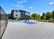 Thumbnail 67 of 71 - A playground area with a blue mat and red circles is surrounded by a fence and a building in the background.