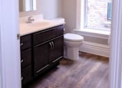 Thumbnail 6 of 9 - A bathroom with a toilet, sink, and wood flooring.