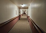 Thumbnail 2 of 11 - A long hallway with a carpeted floor and white walls.