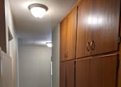 Thumbnail 12 of 15 - A hallway with a refrigerator on the left and wooden cabinets on the right.