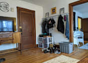 Thumbnail 2 of 9 - A room with a wooden floor and a white wall with a coat rack and a white chair.