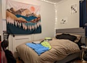 Thumbnail 7 of 9 - A bedroom with a bed, a blanket, a backpack, and a poster on the wall.