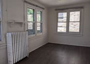 Thumbnail 20 of 29 - A white radiator sits in a room with wooden floors and two windows.